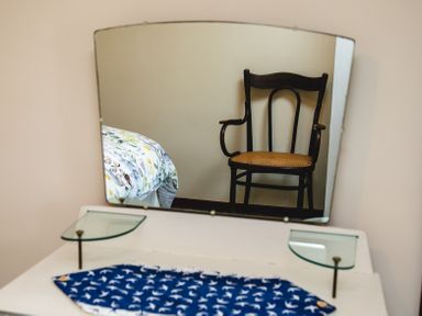 A mirror reflecting a wooden chair with woven seat and a bed with patterned bedding at Swallows Cottage nr Warkworth in Acklington