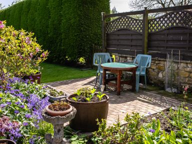 A garden with a wooden table and plastic chairs next to a wooden fence and flowering plants at Swallows Cottage nr Warkworth in Acklington