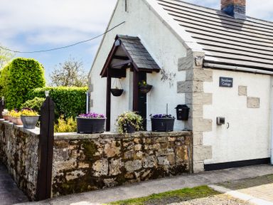 The exterior of a stone cottage with flower pots on a stone wall and a hanging basket at Swallows Cottage nr Warkworth in Acklington