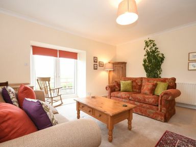 A living room with two sofas a wooden coffee table a rocking chair a tall plant and a wooden cabinet at Dunrovin in Beadnell