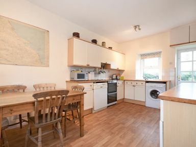 A kitchen with a wooden dining table and chairs a stove dishwasher washing machine and microwave at Dunrovin in Beadnell