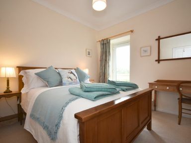 A bedroom with a wooden bed and blue bedding near a wooden desk and chair at Dunrovin in Beadnell