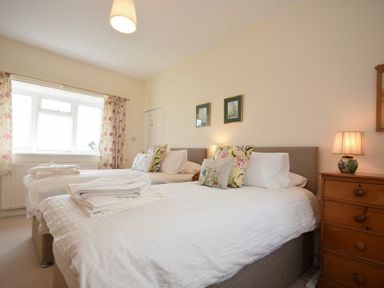 A bedroom with two single beds a wooden dresser with a lamp floral curtains and framed pictures on the wall at Dunrovin in Beadnell