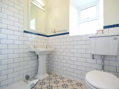 A bathroom with a pedestal sink a toilet white subway tiled walls and a patterned tile floor at Dunrovin in Beadnell