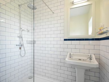 A bathroom with a tiled shower area and a pedestal sink with a mirror above at Dunrovin in Beadnell