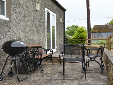 A patio with a charcoal grill wooden bench metal table and chairs next to a building with a glass door Dunrovin Beadnell