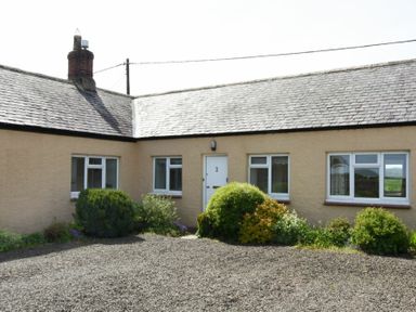 A single story house with beige walls white windows and shrubs in front at Dunrovin in Beadnell