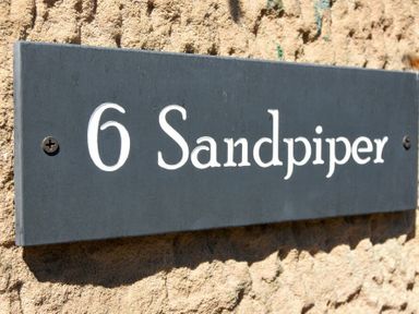 A black house number sign with white text reading 6 Sandpiper on a textured wall at Sandpiper (Alnmouth) in Alnmouth
