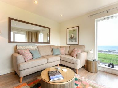 A living room with an L shaped sofa a round coffee table a large window with a sea view and a mirror on the wall at Portside in Seahouses