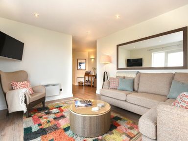 A living room with a beige sofa a round coffee table patterned rug an armchair and a large wall mirror at Portside in Seahouses
