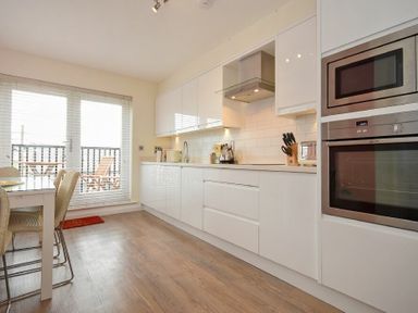 A kitchen with white cabinets a dining table with chairs and a glass door leading to a balcony at Portside in Seahouses
