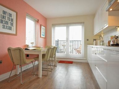 A kitchen and dining area with table and chairs next to large windows and a door leading to a balcony at Portside in Seahouses