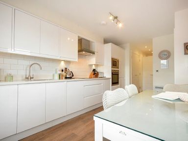 A kitchen with white cabinets a glass dining table with chairs and wooden floor at Portside in Seahouses