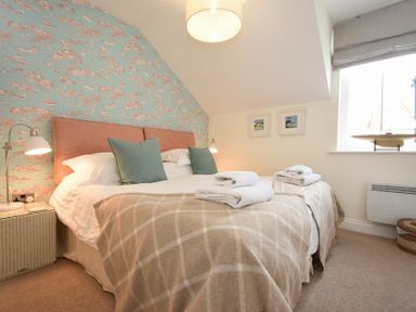 A bedroom with a double bed, bedside lamps, folded towels on the bed, a model boat on the window sill, and framed pictures on the wall at Portside in Seahouses