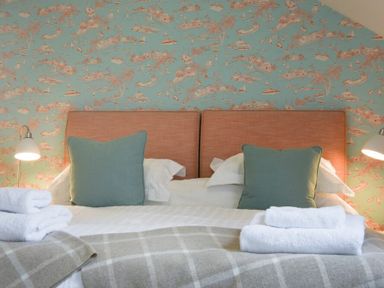 A bed with two brown headboards two green pillows white towels and a pair of lamps on a wallpapered wall at Portside in Seahouses