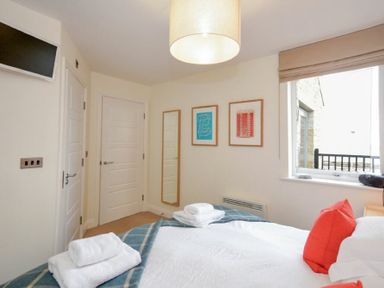 A bedroom with a bed with red pillows and folded towels on a blanket a window with a blind two framed pictures a wall mirror and two white doors at Portside in Seahouses