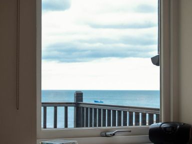 A window showing a balcony railing and a sea view with a boat at Portside in Seahouses