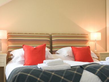 A bedroom with two beds with patterned headboards red pillows white towels and bedside lamps at Portside in Seahouses