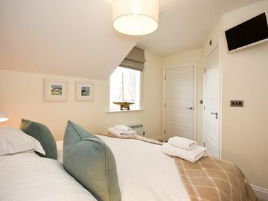 A bedroom with a bed two pillows two doors a window with a model sailboat and a wall-mounted television at Portside in Seahouses