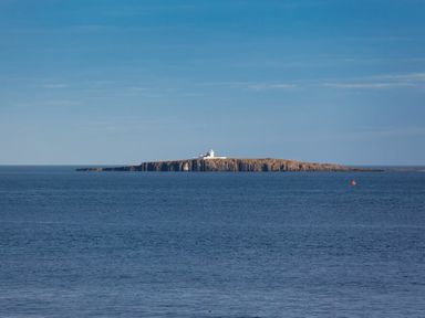 An island with a lighthouse in the middle of a body of water at Portside in Seahouses