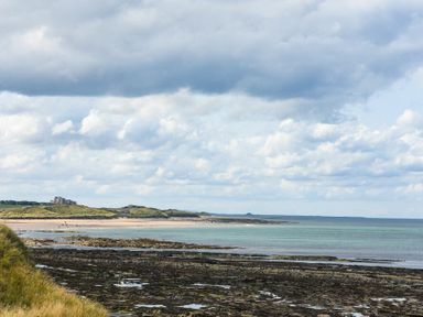 A coastal view with rocky shore and sandy beach with distant dunes at Portside in Seahouses