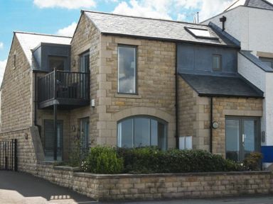 A modern stone house with a balcony and garden in front at Portside in Seahouses