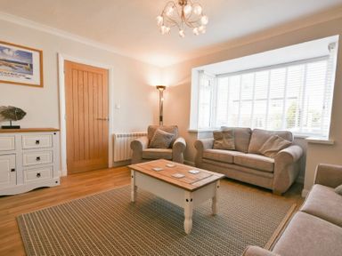 A living room with sofas a wooden coffee table a sideboard and a floor lamp at Anchor Lodge in Seahouses