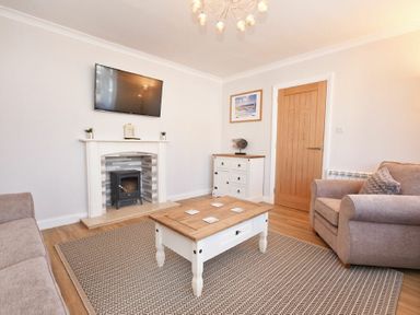 A living room with a wall-mounted TV fireplace coffee table and armchairs at Anchor Lodge in Seahouses