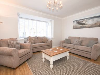 A living room with two sofas an armchair a coffee table and a beach painting at Anchor Lodge in Seahouses