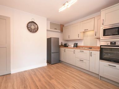 A kitchen with wooden floor cabinets fridge oven microwave wall clock and countertop appliances at Anchor Lodge in Seahouses