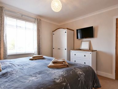 A bedroom with a bed towels on it a wardrobe a chest of drawers and a wall-mounted TV at Anchor Lodge in Seahouses