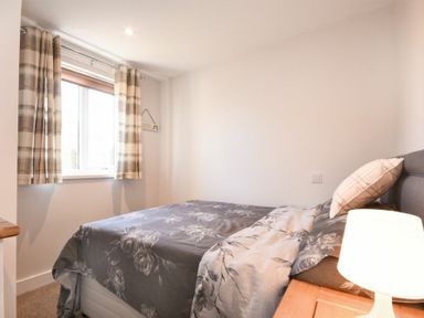 A bedroom with a bed a bedside table and a window with curtains at Anchor Lodge in Seahouses