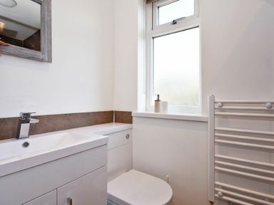 A bathroom with a sink, toilet, window with toiletries, and a heated towel rail at Anchor Lodge in Seahouses