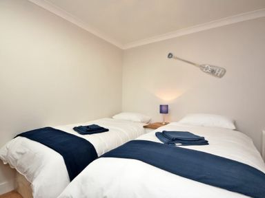 A bedroom with two single beds side by side with navy blue runners and folded towels at Anchor Lodge in Seahouses