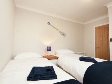 A bedroom with two single beds a wooden bedside table with a lamp and a wooden door at Anchor Lodge in Seahouses