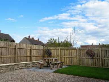 A backyard with a wooden fence a picnic table a gravel area and a small grass patch at Anchor Lodge in Seahouses