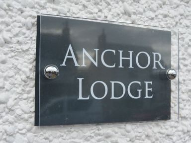 A black sign with white text reading Anchor Lodge mounted on a textured white wall at Anchor Lodge in Seahouses