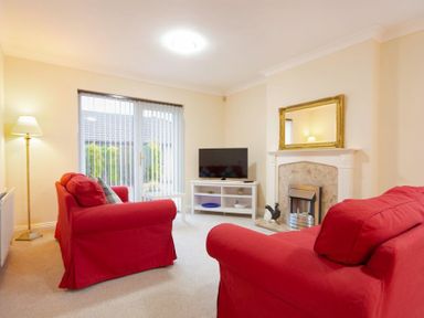 A living room with red sofas a white TV stand and a fireplace with a mirror above at Summerfold in Warkworth