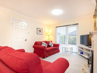 A living room with red sofas a white coffee table a television and vertical blinds at Summerfold in Warkworth