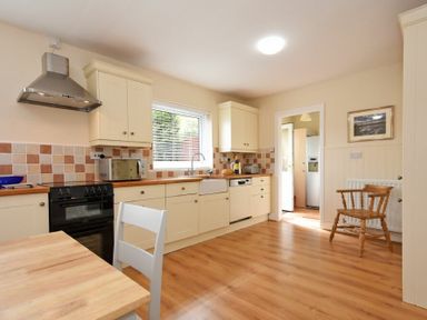 A kitchen with cream cabinets a black stove a wooden chair and a window at Summerfold in Warkworth