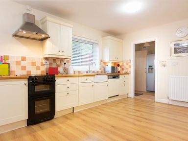 A kitchen with white cabinets wooden countertops a black stove a range hood and a window at Summerfold in Warkworth