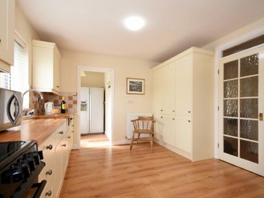 A kitchen with wooden floor cabinets a chair and a refrigerator visible through a doorway at Summerfold in Warkworth