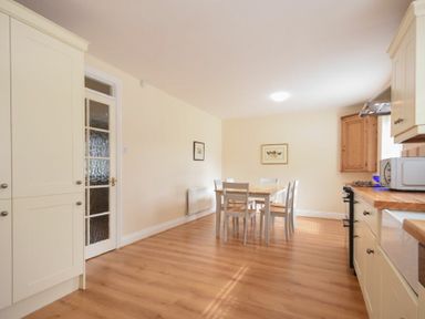 A kitchen with wooden flooring a dining table with chairs cabinets a microwave and a glass paneled door at Summerfold in Warkworth