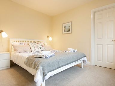 A bedroom with a white bed frame, bedside table, wall lamps, and a framed picture at Summerfold in Warkworth