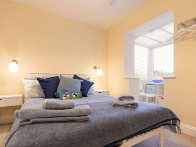 A bedroom with a double bed with pillows and folded towels on it two bedside tables with lamps and a window area with blinds and a chair at Summerfold in Warkworth