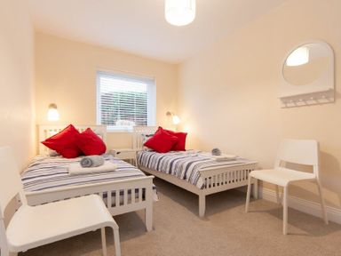 A bedroom with two single beds striped bedding red pillows two white chairs and a window with blinds at Summerfold in Warkworth