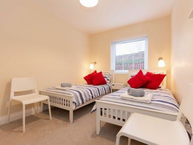 A bedroom with two single beds with striped bedding and red pillows two white chairs and a window at Summerfold in Warkworth