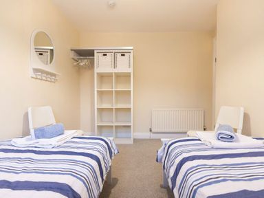 A bedroom with two single beds with striped bedding and a storage unit with baskets at Summerfold in Warkworth