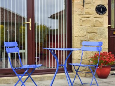 A small patio with a blue metal table and two matching chairs outside a stone building at Summerfold in Warkworth