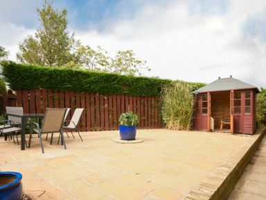 An outdoor patio with a dining table and chairs a potted plant and a wooden gazebo at Summerfold in Warkworth
